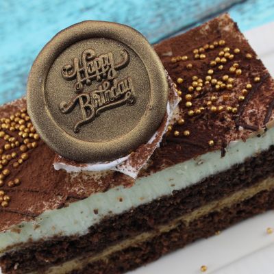 Köstliches Stück Schokoladenkuchen mit Schokolade und goldenem „Happy Birthday“-Aufleger